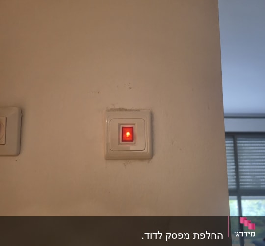מתג חשמלי עם נורית חיווי אדומה על קיר